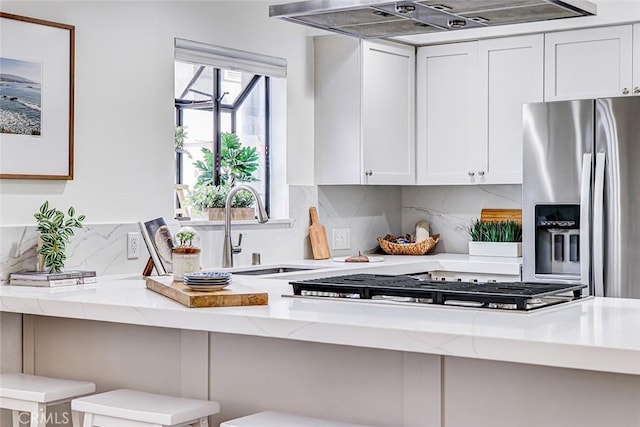 kitchen with extractor fan, light stone counters, white cabinets, stainless steel fridge, and a sink