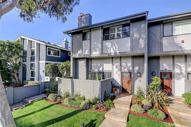 view of front of property with stucco siding, a chimney, a front lawn, and fence