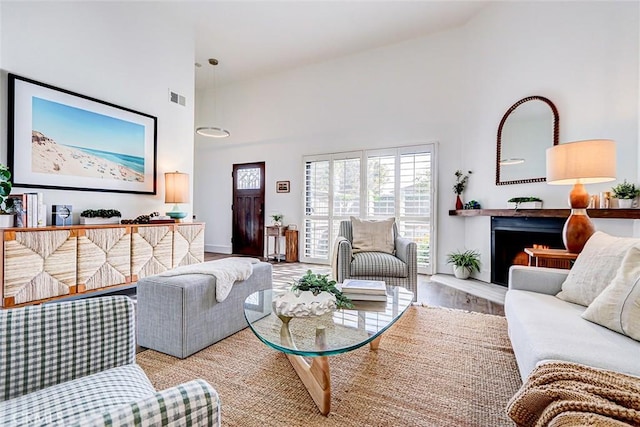 living area with visible vents, high vaulted ceiling, a fireplace with raised hearth, and wood finished floors