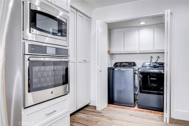 clothes washing area with cabinet space, separate washer and dryer, and light wood-style flooring