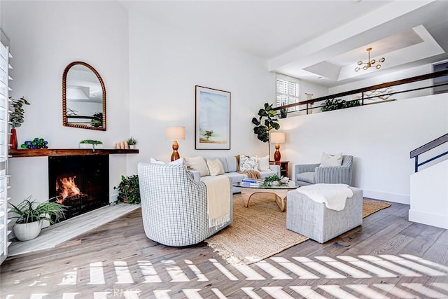 living room featuring baseboards, a lit fireplace, wood finished floors, a notable chandelier, and a raised ceiling