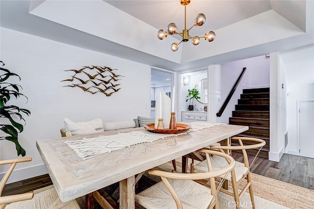 dining room featuring a chandelier, stairway, a raised ceiling, and wood finished floors