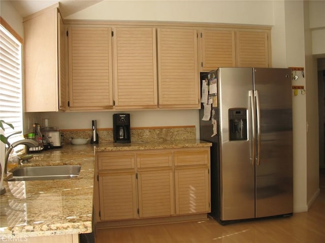 kitchen with light wood-style flooring, stainless steel fridge with ice dispenser, light stone countertops, and a sink