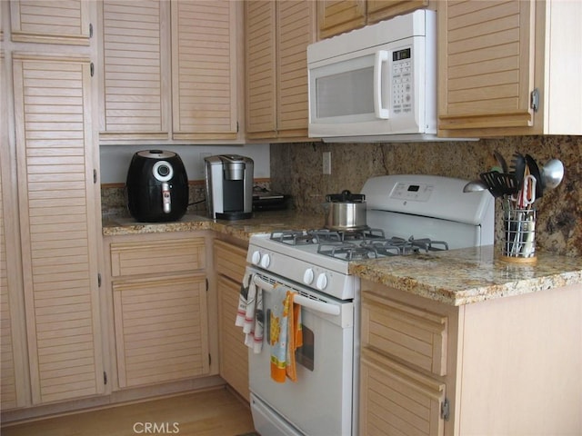 kitchen featuring decorative backsplash, white appliances, and light stone countertops