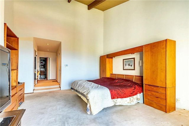 bedroom featuring beam ceiling, light colored carpet, and a high ceiling