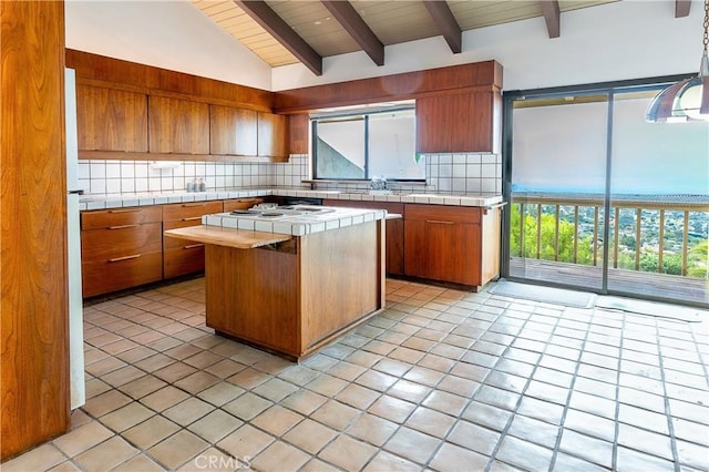 kitchen featuring tasteful backsplash, vaulted ceiling with beams, brown cabinetry, and tile counters