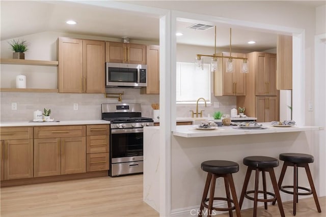 kitchen featuring visible vents, a breakfast bar, light countertops, appliances with stainless steel finishes, and open shelves