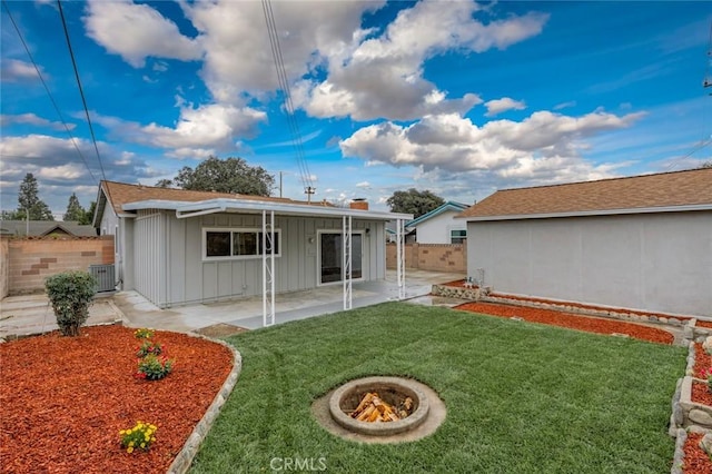 back of property with a lawn, a patio, an outdoor fire pit, fence, and board and batten siding