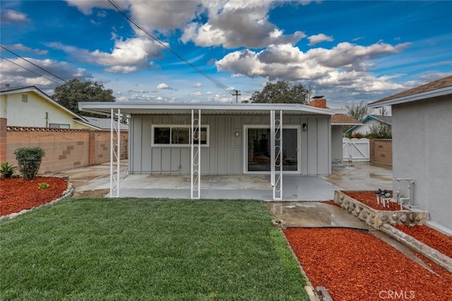 rear view of house featuring board and batten siding, a lawn, a chimney, a patio, and a gate