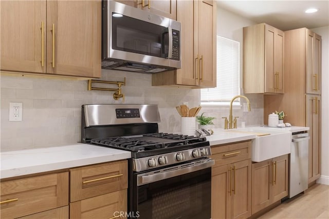 kitchen featuring light stone counters, light brown cabinets, a sink, stainless steel appliances, and backsplash