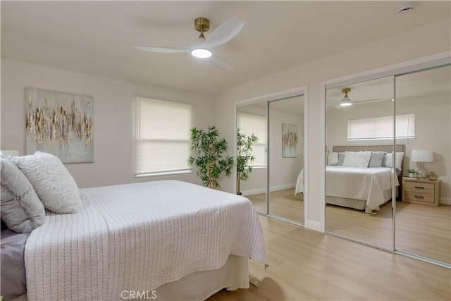 bedroom featuring baseboards, two closets, ceiling fan, and light wood finished floors