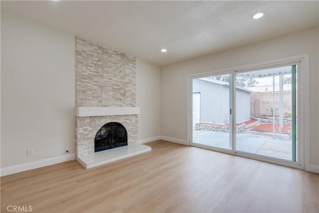 unfurnished living room featuring recessed lighting, baseboards, a stone fireplace, and wood finished floors