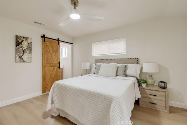 bedroom featuring a ceiling fan, baseboards, light wood finished floors, visible vents, and a barn door