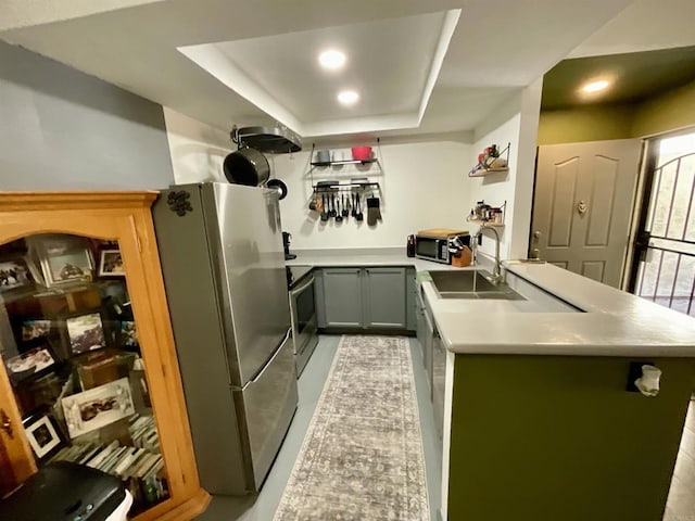 kitchen with a sink, a tray ceiling, appliances with stainless steel finishes, a peninsula, and light countertops