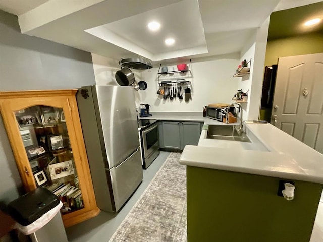 kitchen featuring a peninsula, a sink, stainless steel appliances, light countertops, and a raised ceiling