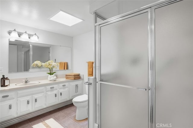 bathroom with vanity, a skylight, a shower stall, tile patterned floors, and toilet