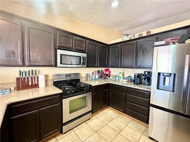 kitchen with light stone counters, a textured ceiling, appliances with stainless steel finishes, light tile patterned floors, and dark brown cabinets