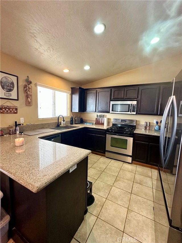 kitchen featuring a sink, stainless steel appliances, a peninsula, light tile patterned floors, and lofted ceiling