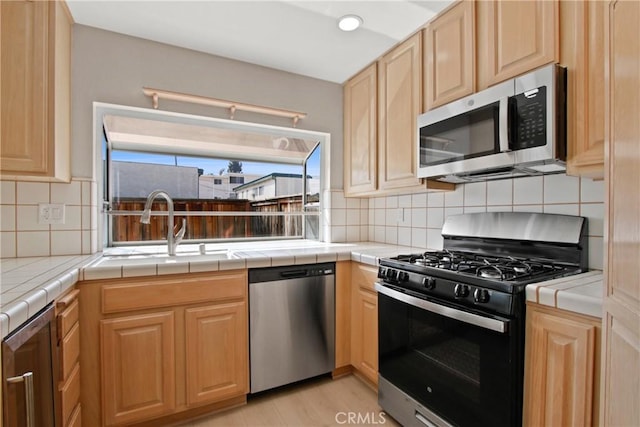 kitchen with light brown cabinetry, tile countertops, stainless steel appliances, and tasteful backsplash