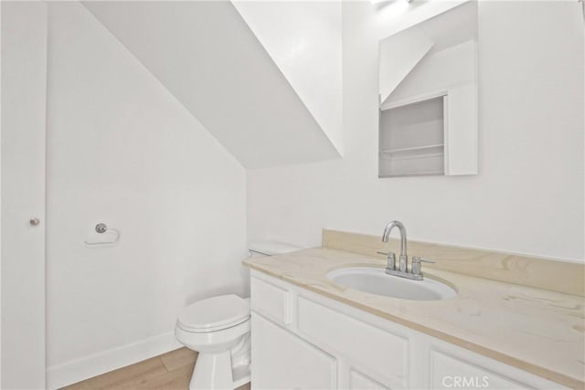 bathroom with toilet, vanity, baseboards, and wood finished floors