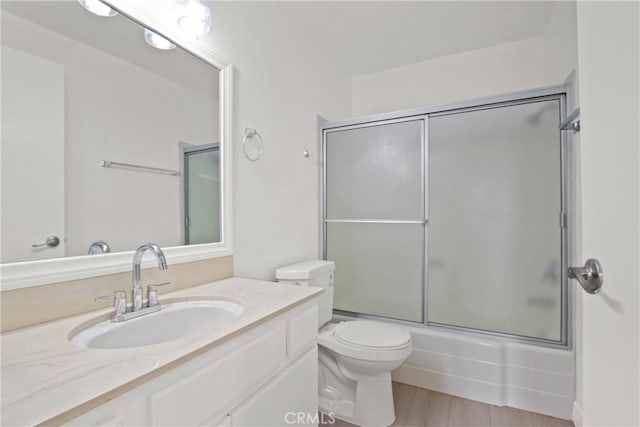 bathroom featuring wood finished floors, toilet, vanity, and bath / shower combo with glass door