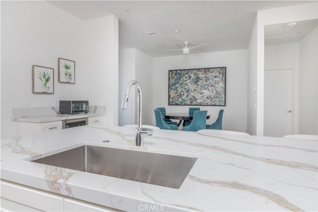 kitchen featuring a ceiling fan, light stone counters, a sink, open floor plan, and white cabinets