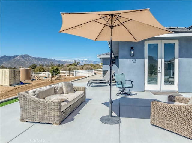 view of patio with a mountain view, outdoor lounge area, french doors, and fence