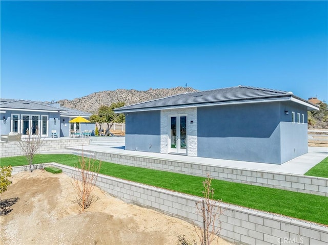 rear view of property with stucco siding, fence, french doors, a mountain view, and a tiled roof