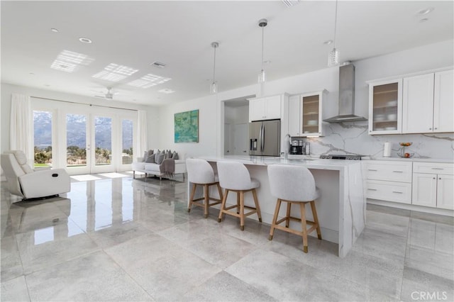 kitchen with a kitchen island with sink, light countertops, stainless steel refrigerator with ice dispenser, wall chimney exhaust hood, and open floor plan