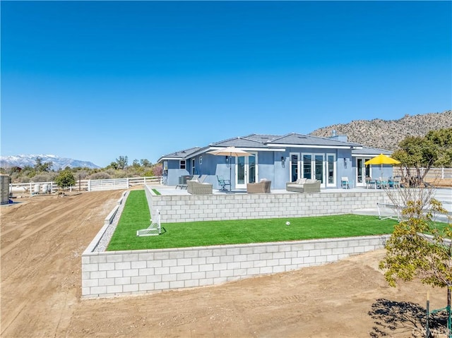 rear view of house featuring a mountain view, stucco siding, fence private yard, a patio area, and a lawn