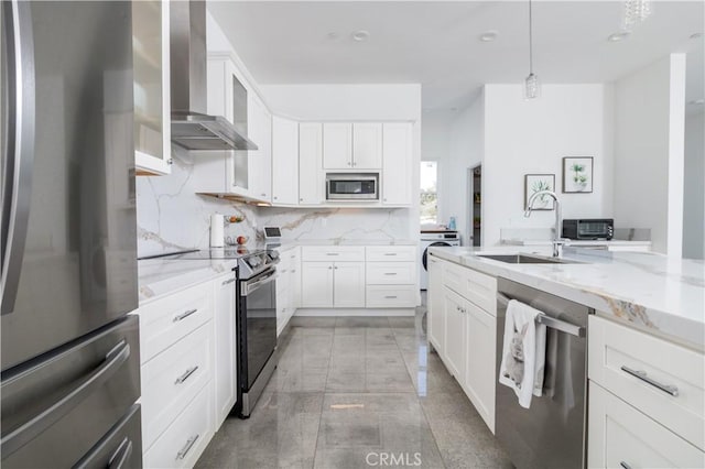 kitchen with a sink, light stone counters, stainless steel appliances, wall chimney range hood, and decorative backsplash