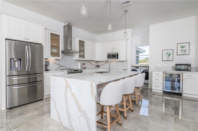 kitchen featuring beverage cooler, visible vents, stainless steel appliances, exhaust hood, and washing machine and dryer