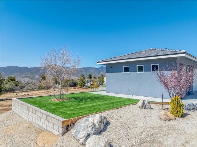 view of side of home with a lawn, a mountain view, and stucco siding