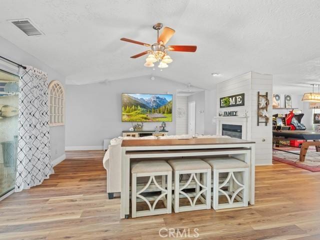 living area featuring visible vents, lofted ceiling, ceiling fan, and light wood-style flooring