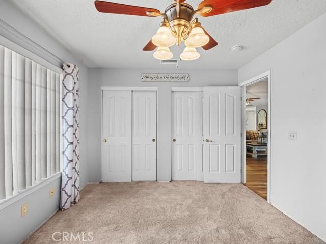 unfurnished bedroom featuring carpet flooring, a textured ceiling, two closets, and visible vents