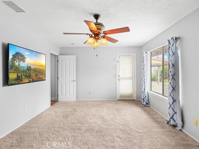 carpeted empty room with visible vents, a textured ceiling, and a ceiling fan