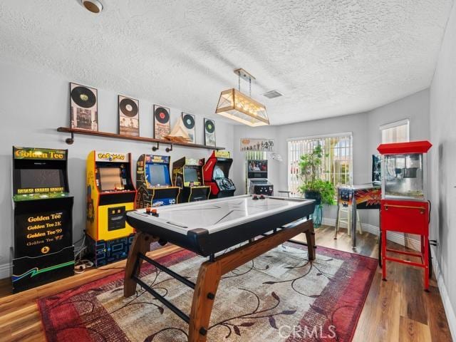 rec room with baseboards, wood finished floors, visible vents, and a textured ceiling