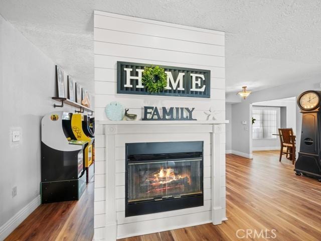 details with a glass covered fireplace, a textured ceiling, baseboards, and wood finished floors