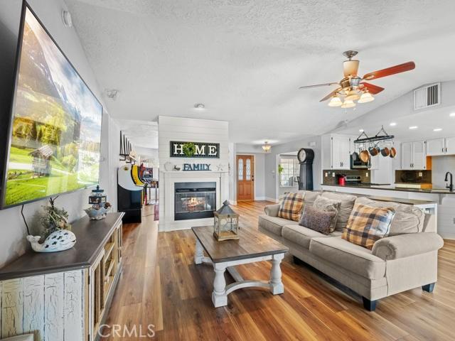 living area with visible vents, vaulted ceiling, wood finished floors, a textured ceiling, and a ceiling fan