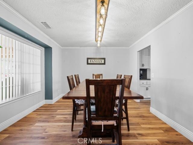 dining room with crown molding, baseboards, visible vents, and light wood-type flooring