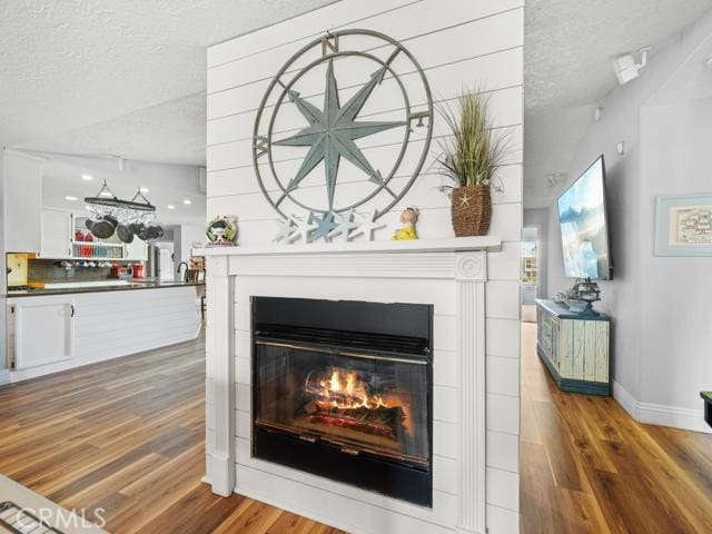 interior details featuring a glass covered fireplace, wood finished floors, baseboards, and a textured ceiling