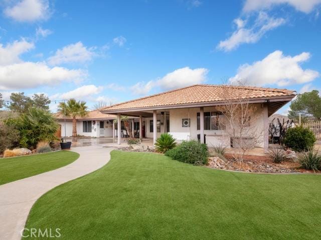 back of property with a tiled roof, a yard, and stucco siding