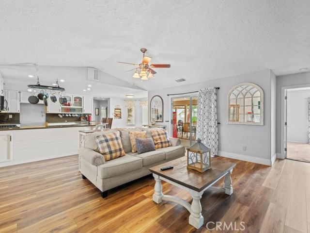 living area with light wood finished floors, visible vents, ceiling fan, vaulted ceiling, and a textured ceiling