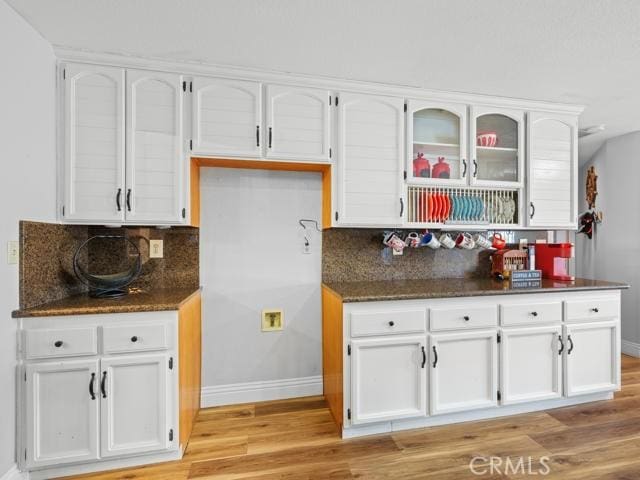 kitchen featuring baseboards, light wood finished floors, decorative backsplash, glass insert cabinets, and white cabinetry