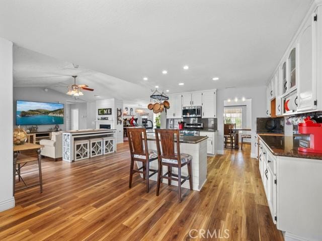 kitchen with a ceiling fan, stainless steel microwave, dark countertops, and light wood-type flooring