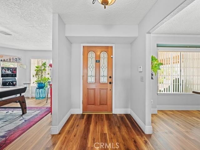 foyer featuring visible vents, a textured ceiling, baseboards, and wood finished floors