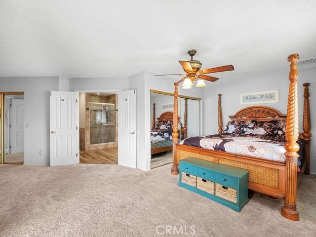 carpeted bedroom with ensuite bathroom, a ceiling fan, and two closets