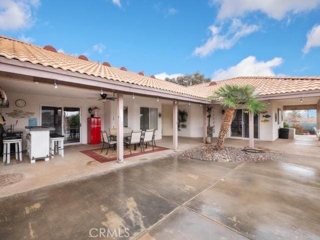 back of house with ceiling fan, stucco siding, a tile roof, a patio area, and outdoor dry bar