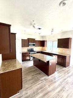 kitchen with dark brown cabinets, light wood finished floors, appliances with stainless steel finishes, and a center island