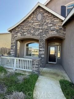 doorway to property featuring stucco siding, stone siding, and a porch